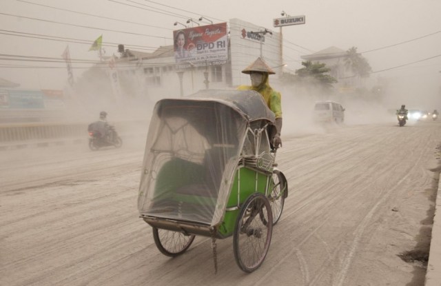 a man rides is becak through the falling ash (Reuters) (click for more photos from the Jakarta Globe)