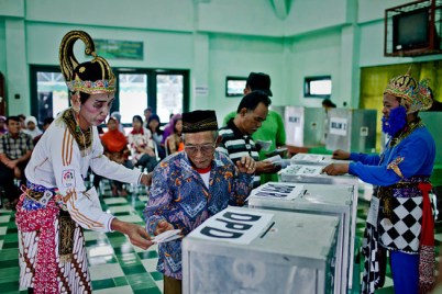 An election officer in traditional shadow puppet costume helps an elderly man vote at  in Yogyakarta (photo: the Wall Street Journal)
