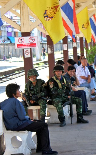 Soldiers at the Phitsanulok train station in Northern Thailand, under the flags of Thailand and the monarchy.